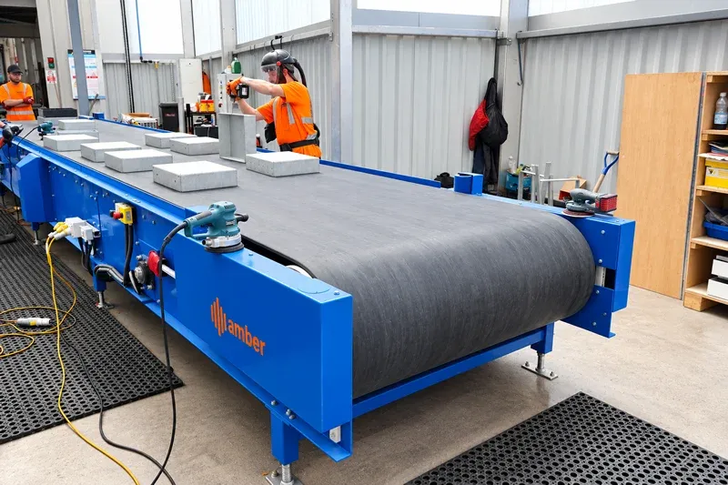 Amber Industries industrial belt conveyor transporting concrete components in a manufacturing facility