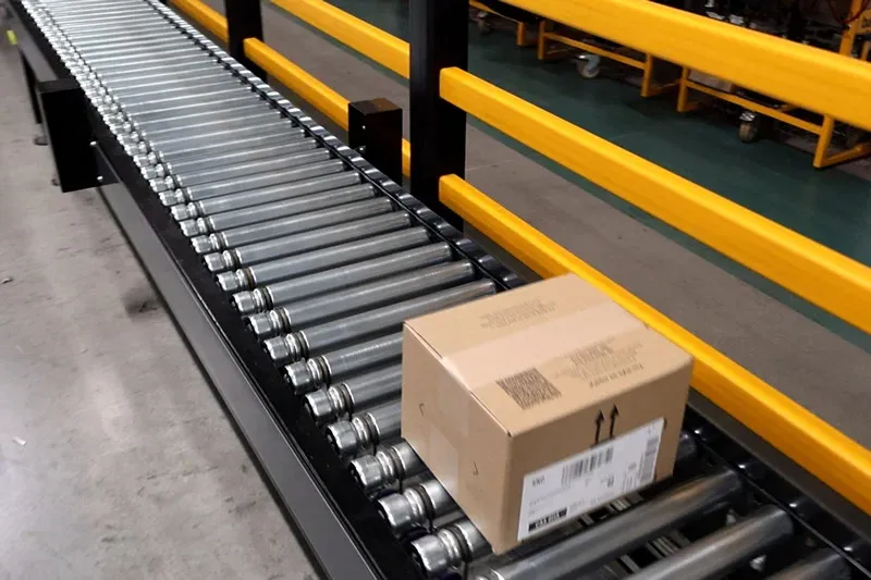 Straight lineshaft roller conveyor transporting a cardboard carton alongside protective barriers