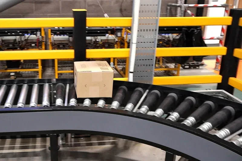 Carton travelling around a powered roller conveyor bend with yellow safety barriers